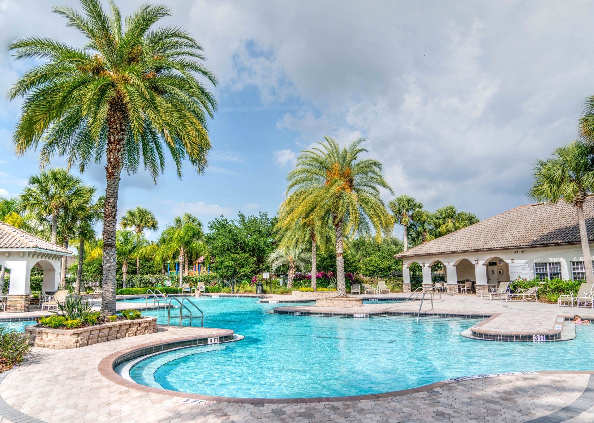Palm-lined resort pool with turquoise water, curved stone edge, and white cabanas under a blue sky