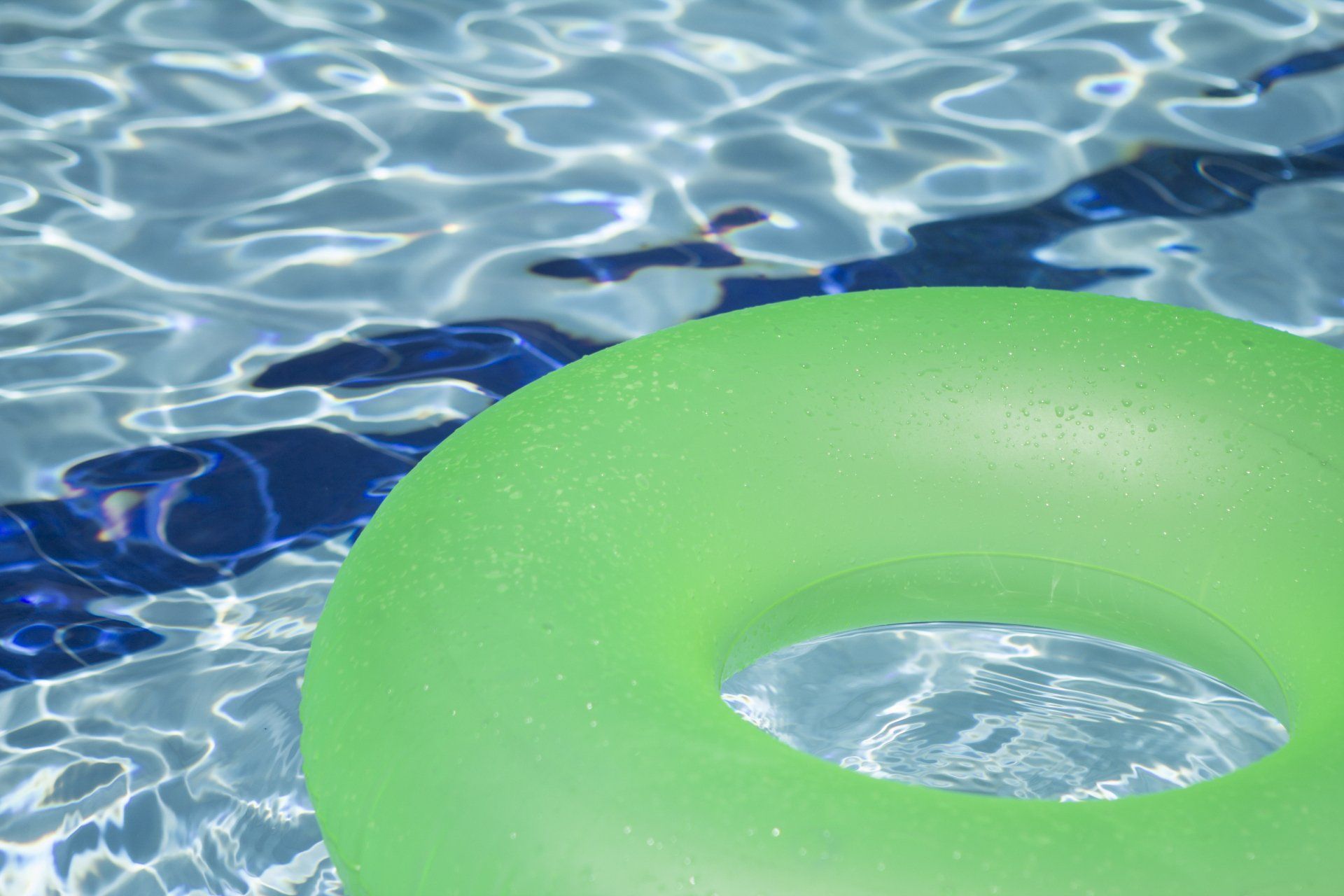 Green inflatable swim ring floating on rippling blue pool water
